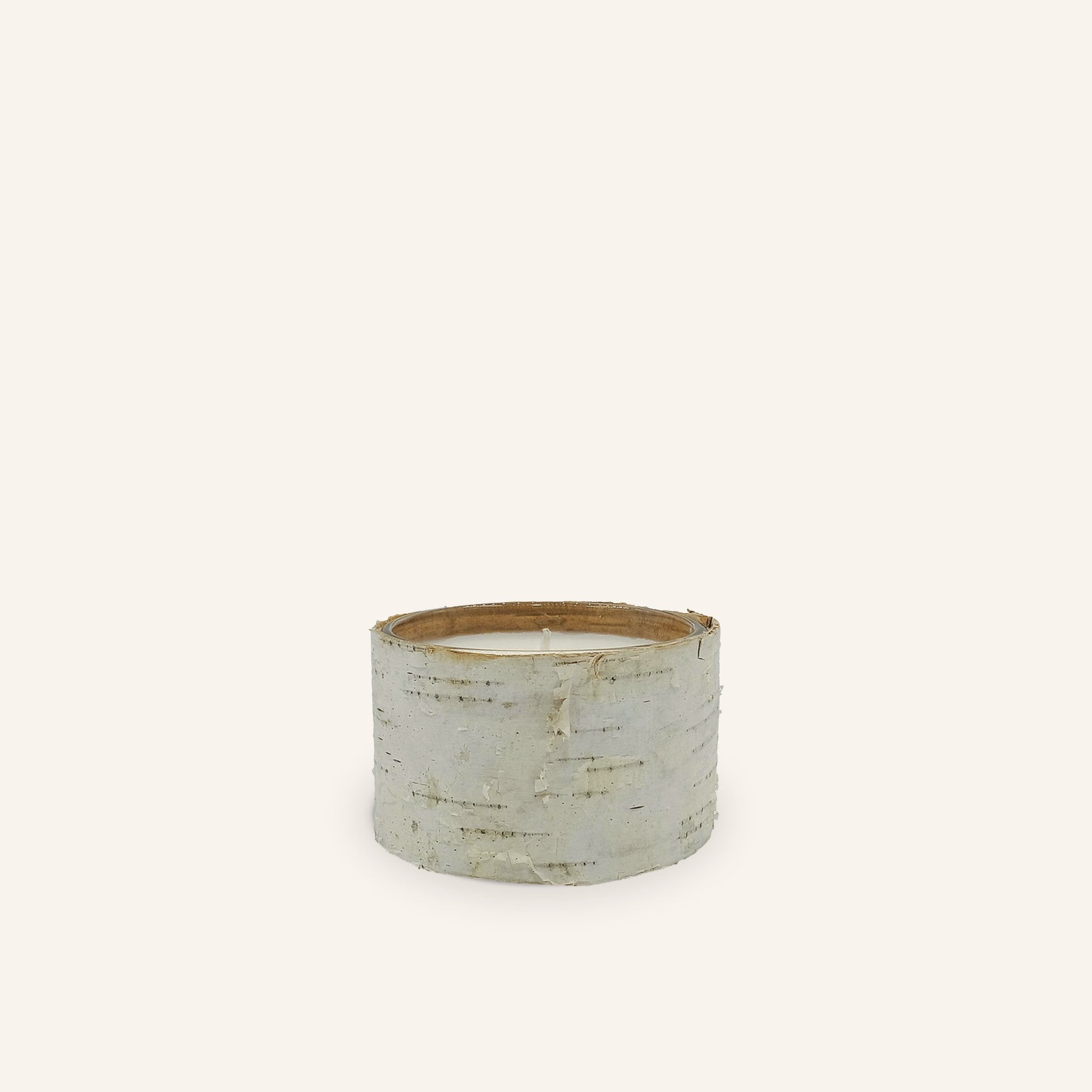 The Birch Filled candle is a white wax candle with birch bark around the outside. This candle has a tag tied with rope that reads, "Red Leaf Home. Birch Bark. Hand crafted in Thailand."