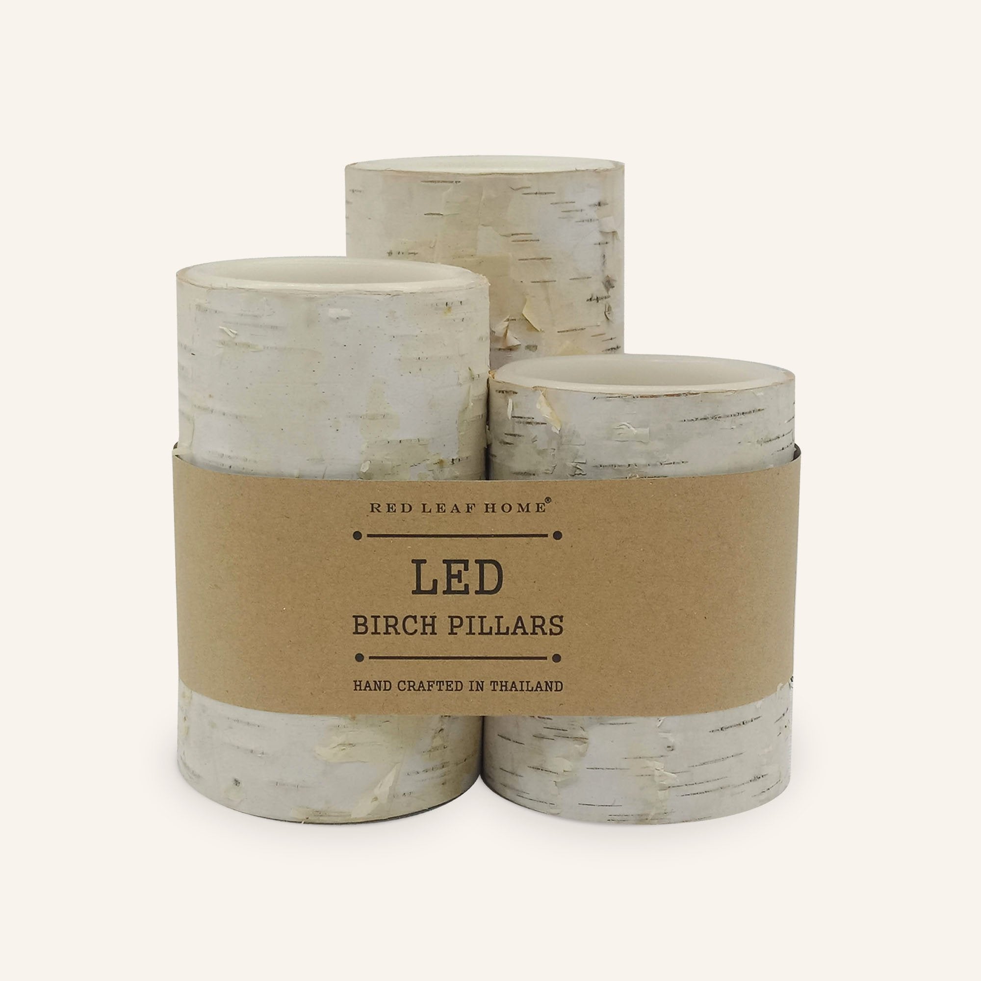 Three birch-bark LED candles wrapped in a brown paper label that reads, "Red Leaf Home. LED Birch Pillars. Hand crafted in Thailand."